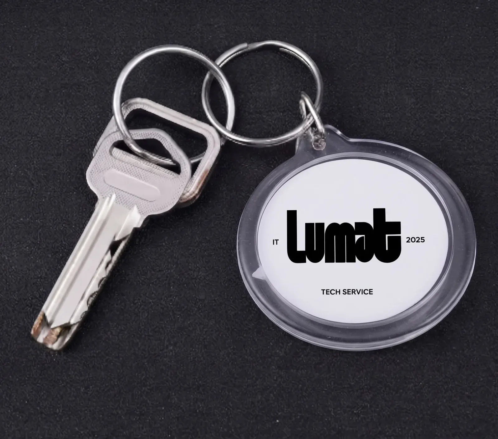 Portachiavi rotondo trasparente con logo stampato su fondo bianco, appeso a un anello insieme a una chiave